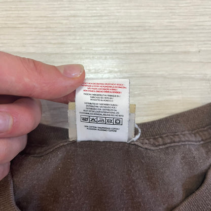 Close-up of a clothing label on brown fabric with a hand holding it.