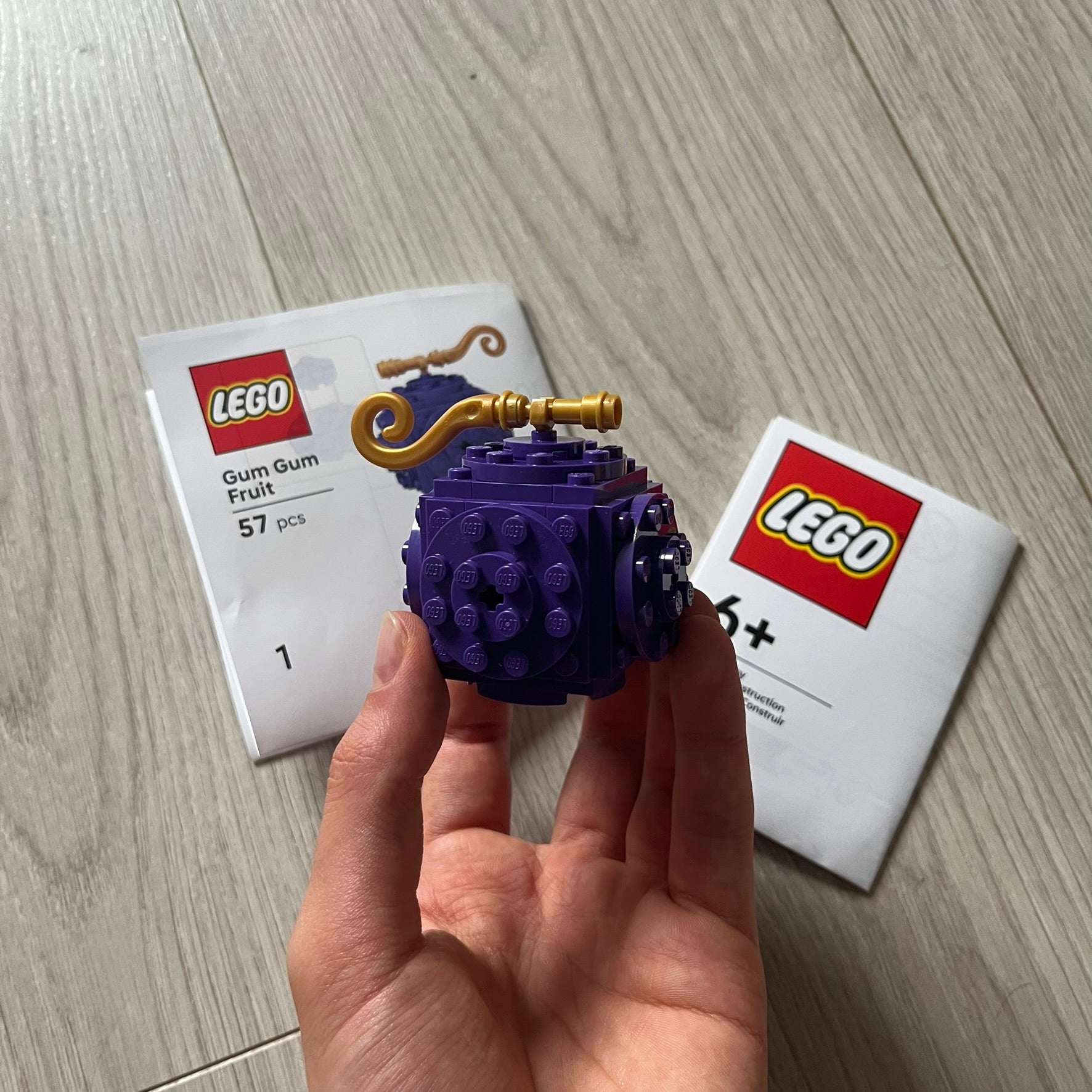 Purple LEGO model held in a hand with LEGO packaging in the background