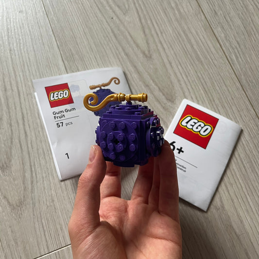Purple LEGO model held in a hand with LEGO packaging in the background