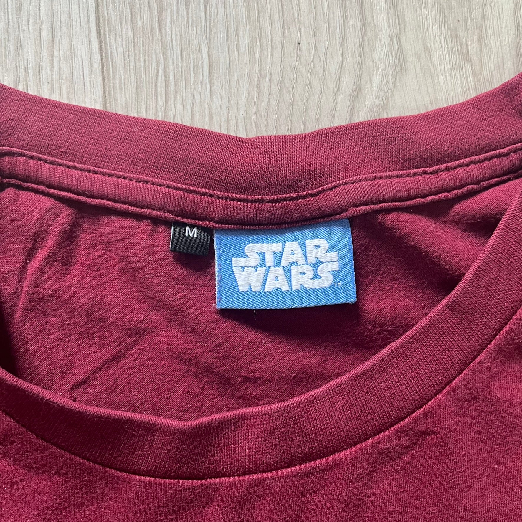 Maroon shirt with a Star Wars tag on a wooden surface