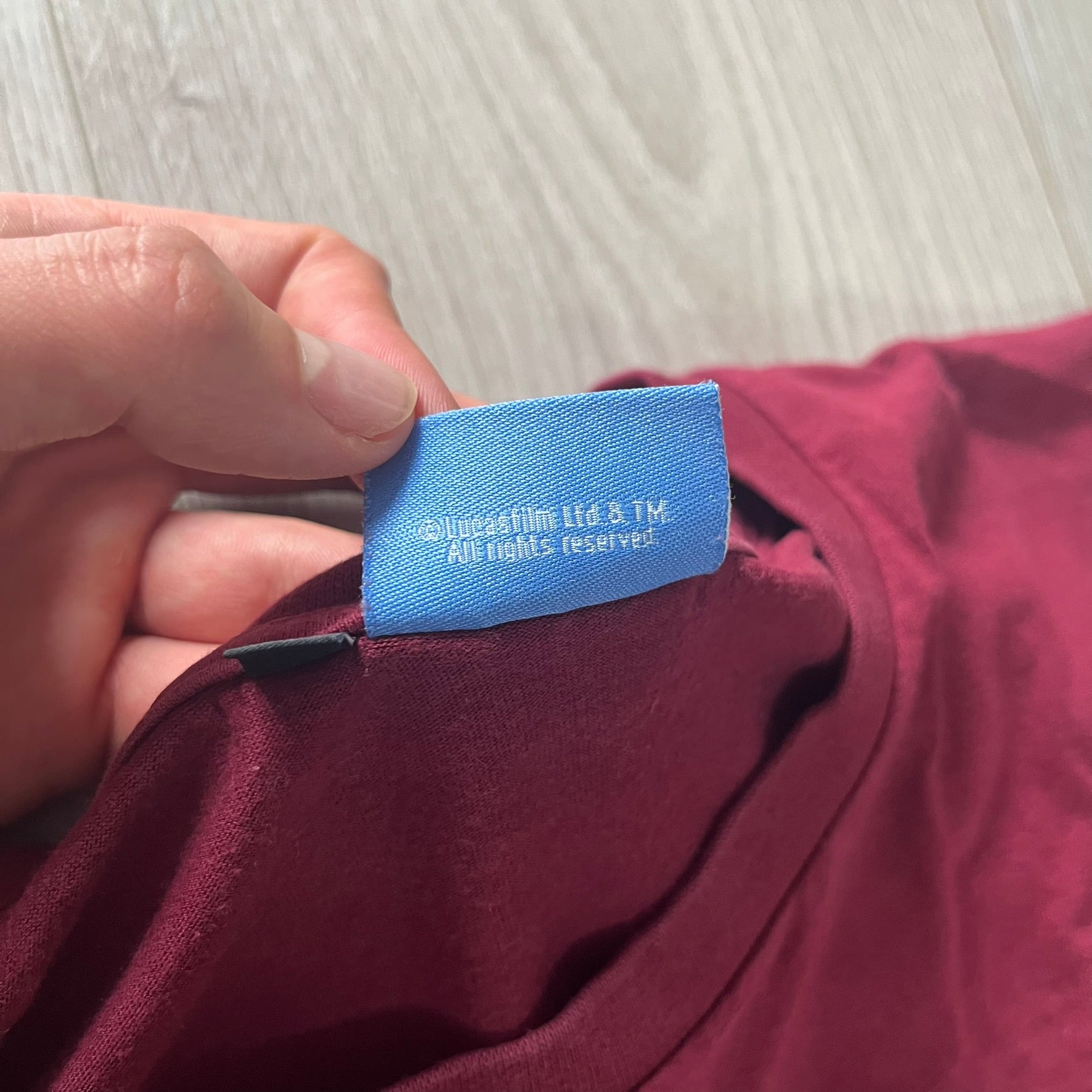 Hand holding a blue label on a maroon garment with a light wooden surface in the background