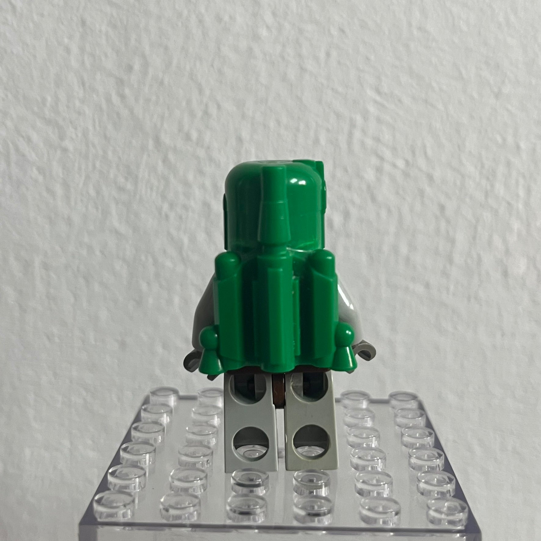 Green toy figure on a clear baseplate against a white background