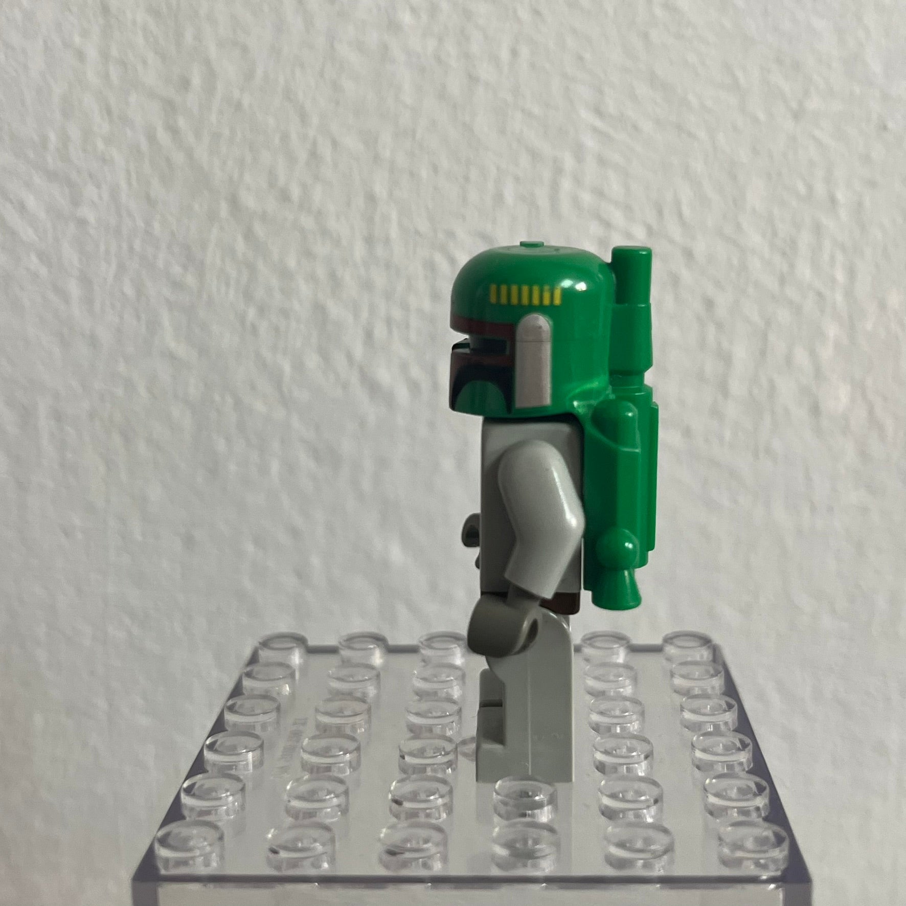 Green and gray robot figure on a clear base against a white wall