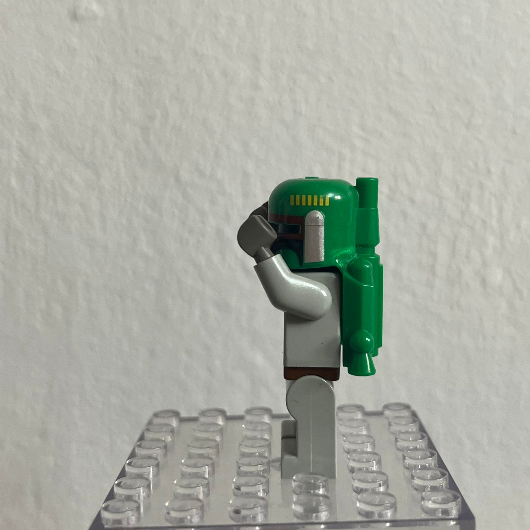 Green and gray Lego figure on a clear baseplate against a white background
