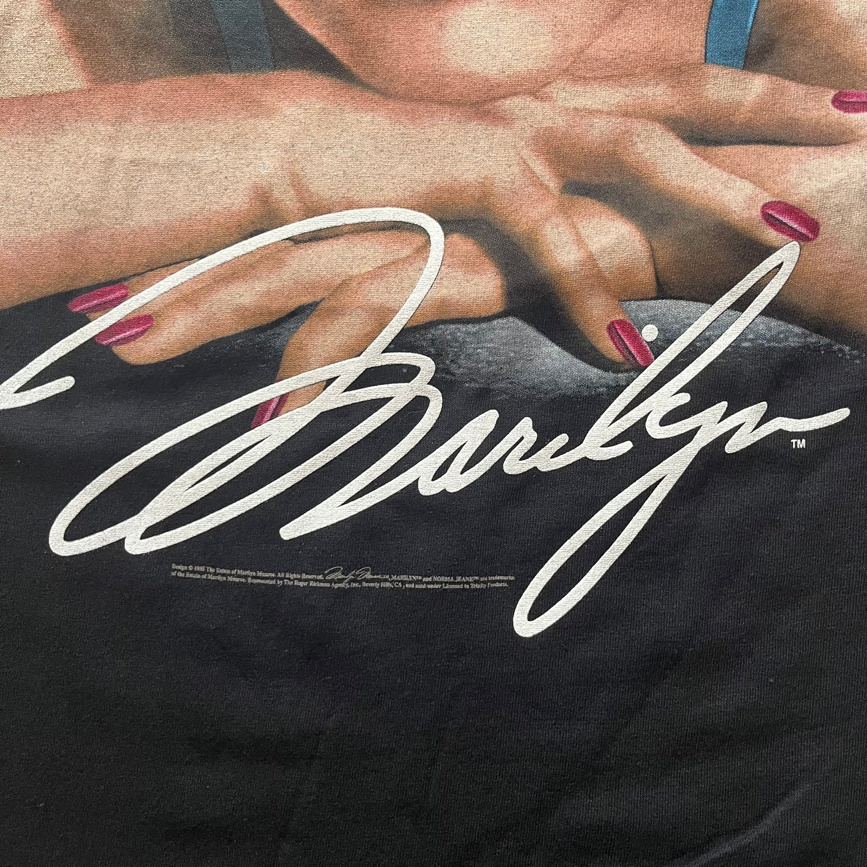Close-up of a black shirt with a signature and hands wearing red nail polish.
