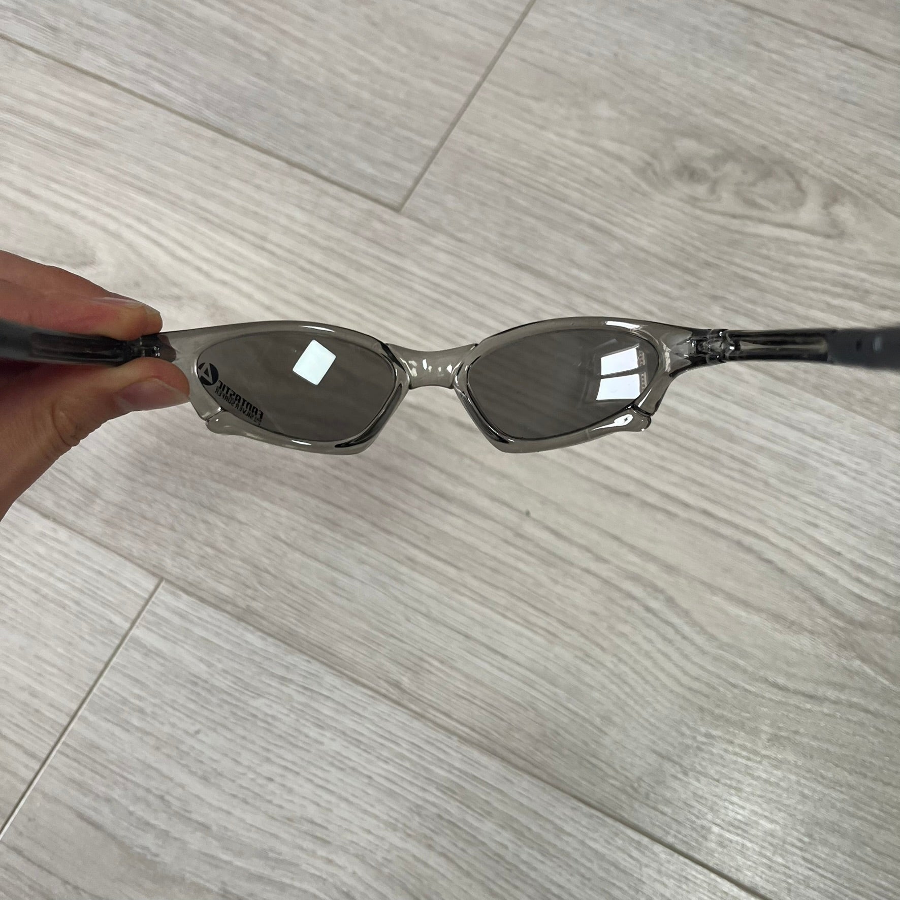 Sunglasses held by a hand on a wooden floor