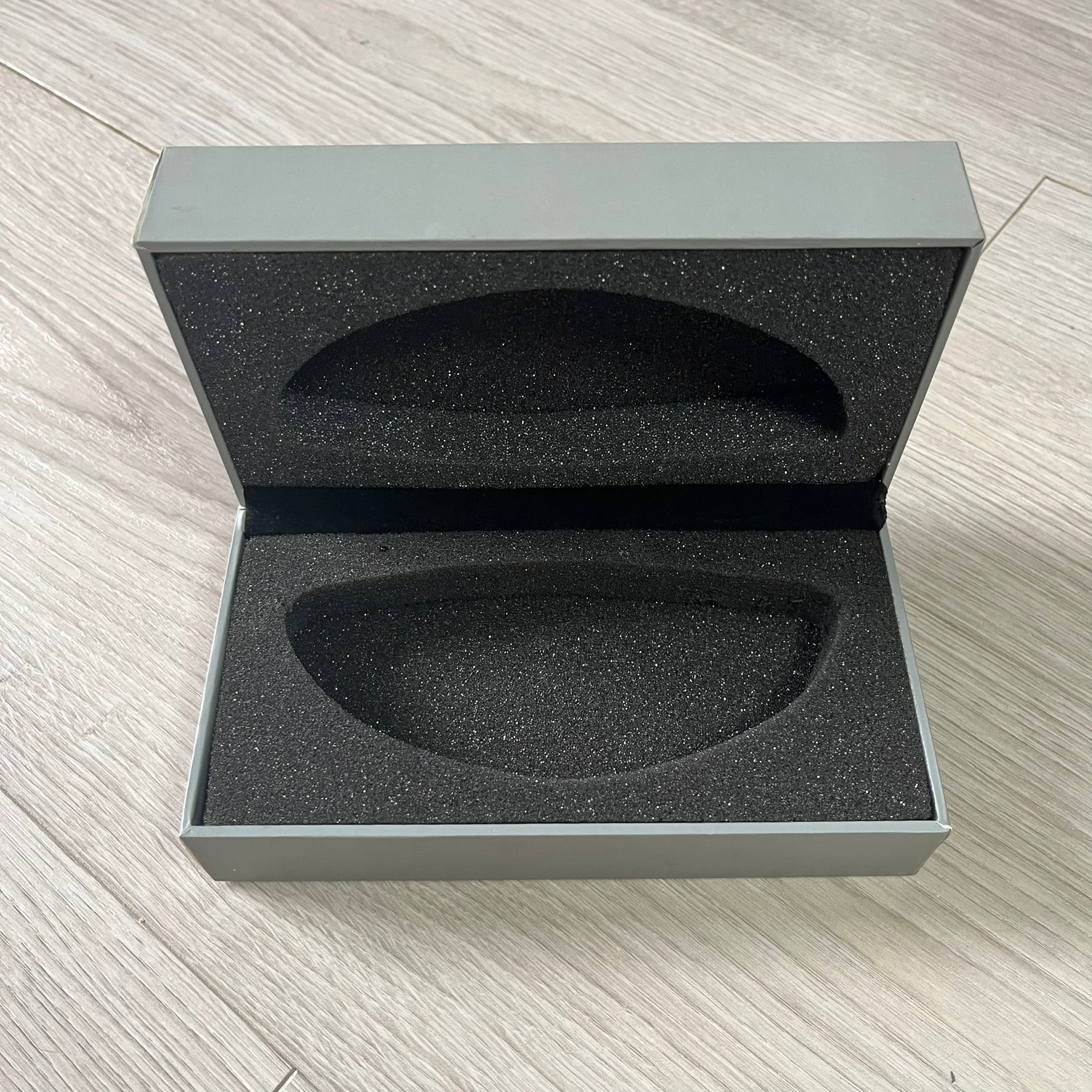 Open gray box with black interior foam on a light wooden surface