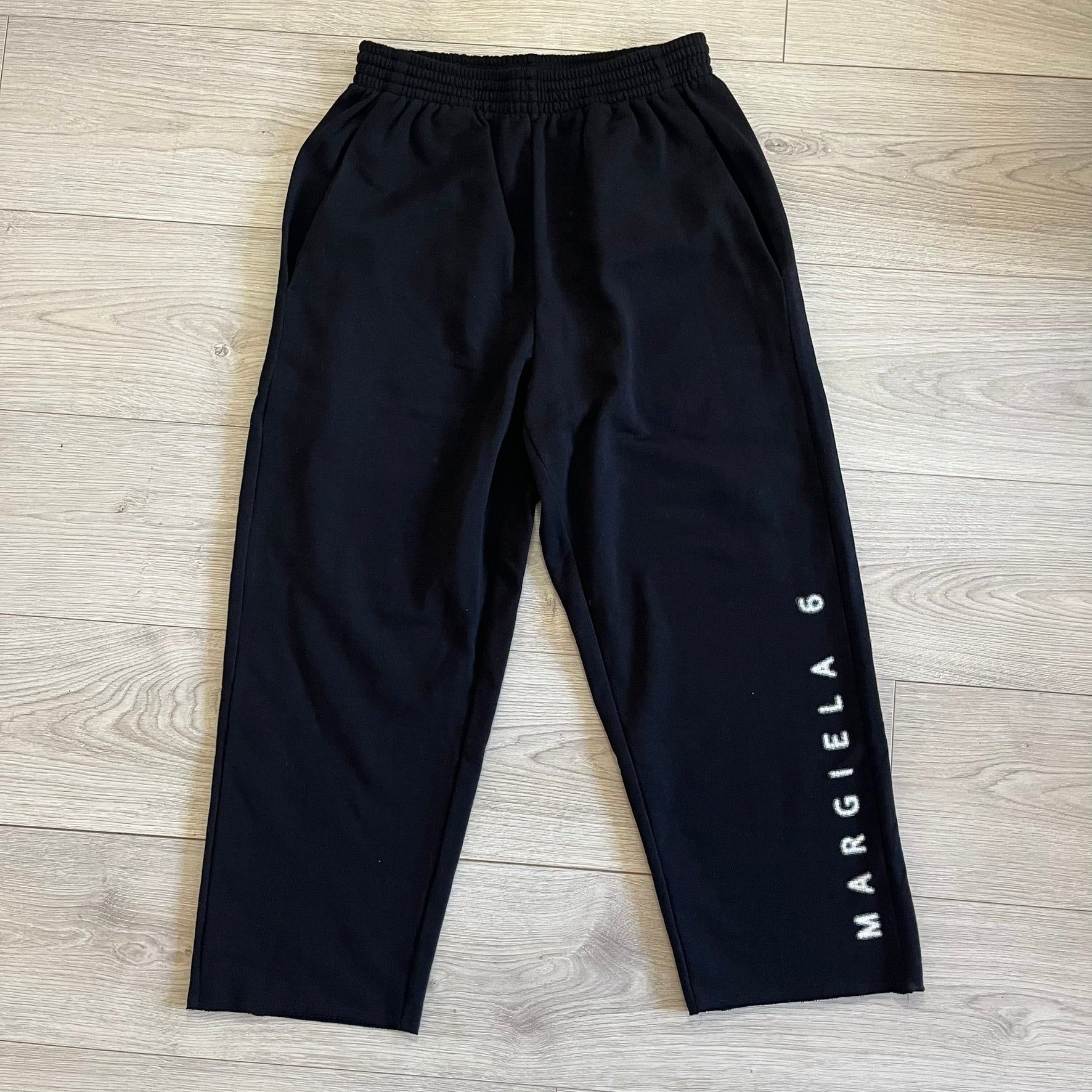 Black pants with 'MARGIELA 6' branding on a wooden floor