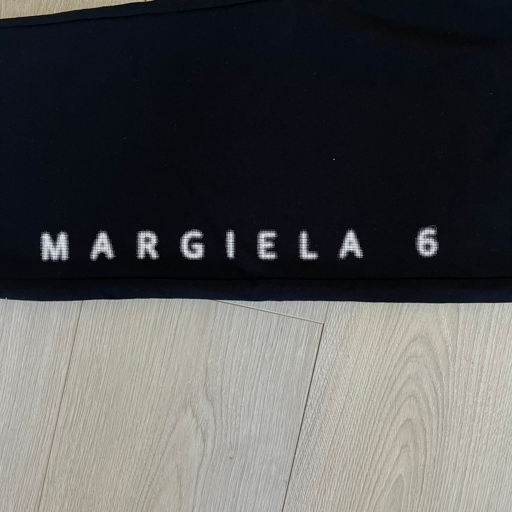Black fabric with 'MARGIELA 6' text on a wooden surface