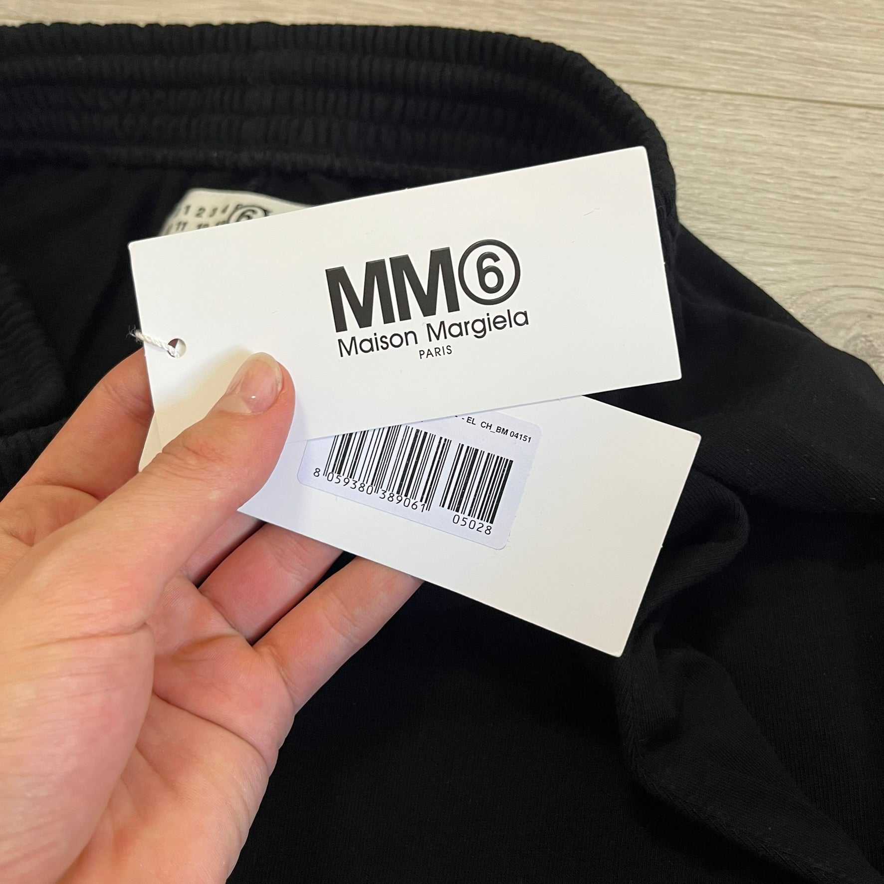 Hand holding a Maison Margiela tag with black text on a dark fabric background
