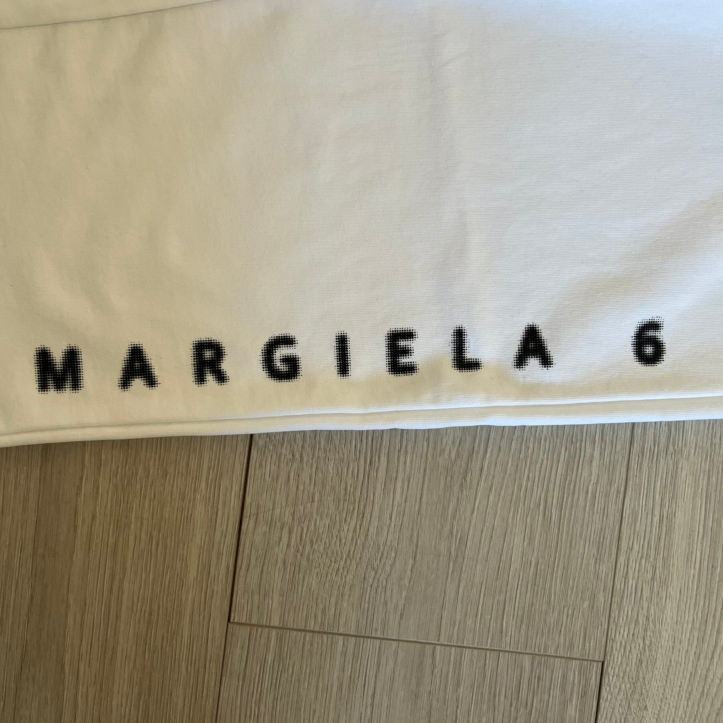 Beige fabric with 'MARGIELA 6' printed on it, on a wooden floor.