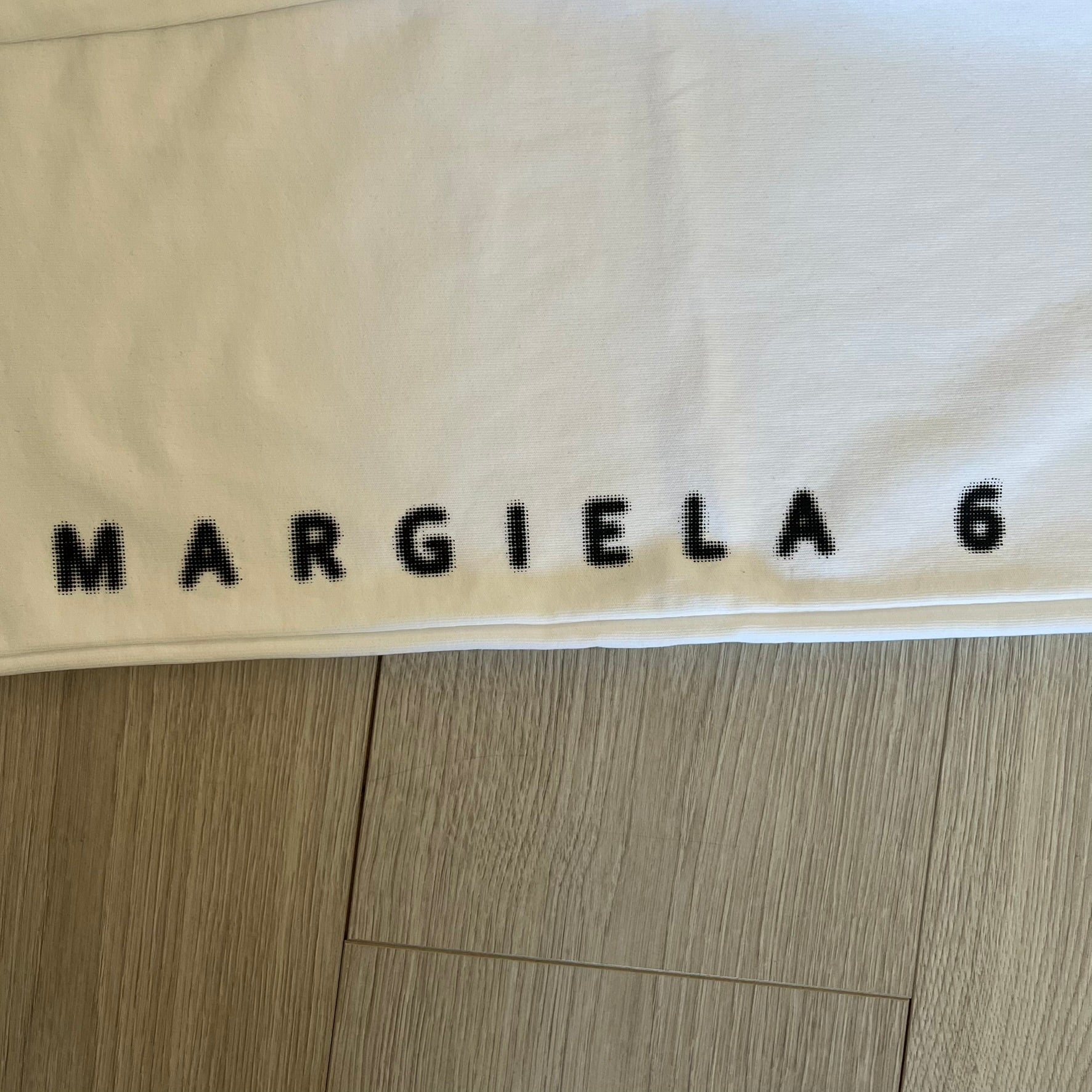 Beige fabric with 'MARGIELA 6' printed on it, on a wooden floor.