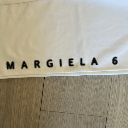 Beige fabric with 'MARGIELA 6' printed on it, on a wooden floor.