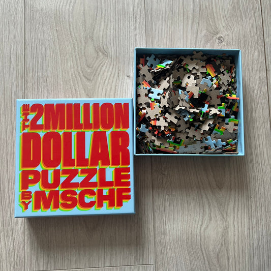 Jigsaw puzzle with box labeled '2 Million Dollar Puzzle by MSCHF' on a wooden surface