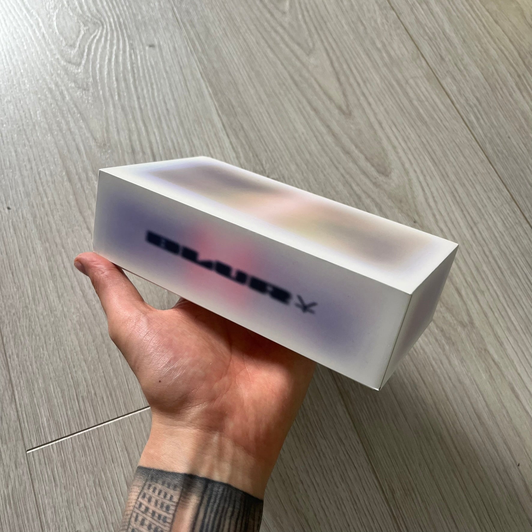 Hand holding a white rectangular box with text on a wooden floor