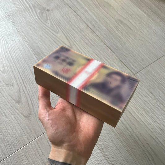 Hand holding a rectangular box with a reflective surface on a wooden floor.
