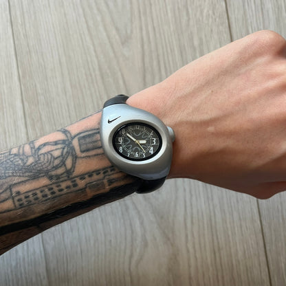 Wrist wearing a unique watch with a tattooed arm on a wooden surface