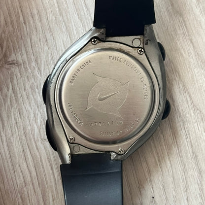 Back view of a watch with a brand logo on a wooden surface