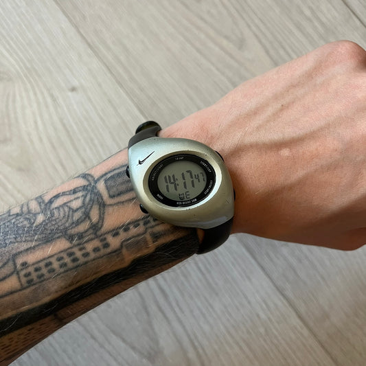 Digital watch on a wrist with a tattooed arm, on a light wooden surface