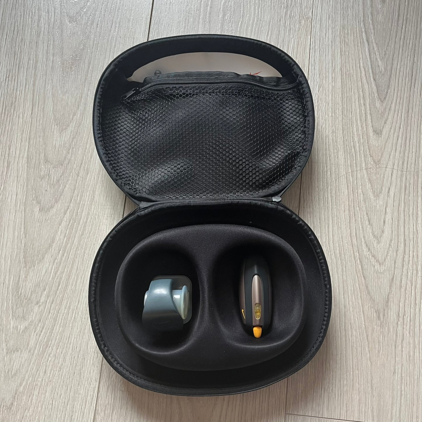 Black carrying case with two hearing aids on a wooden floor.