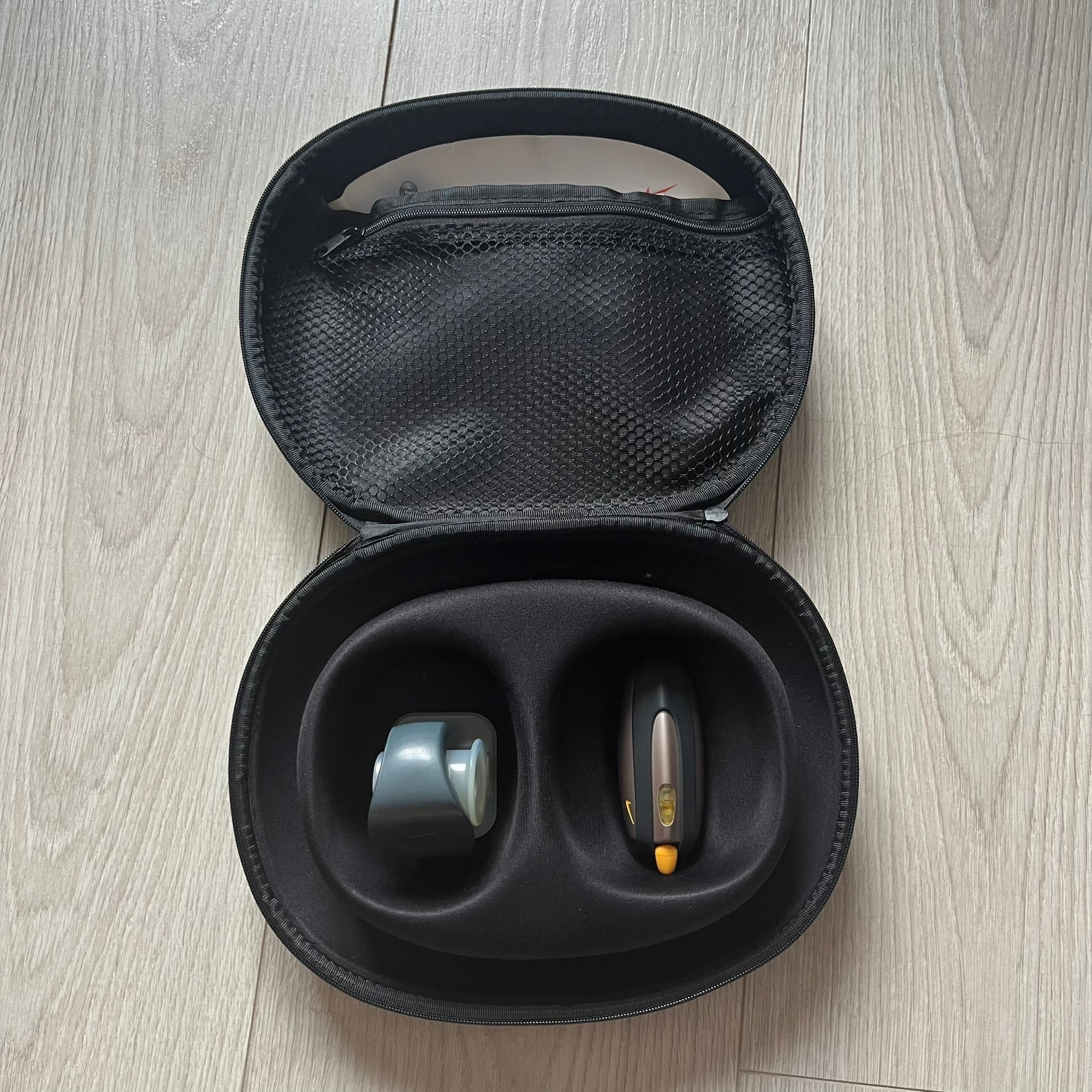 Black carrying case with two hearing aids on a wooden floor.