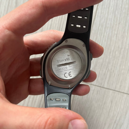 Hand holding a smartwatch with a visible backside label on a light background