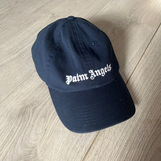 Navy blue cap with 'Palm Angels' logo on a light wooden floor