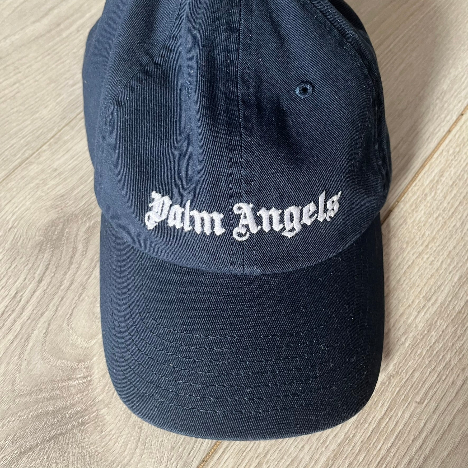 Navy blue cap with 'Palm Angels' logo on a wooden surface