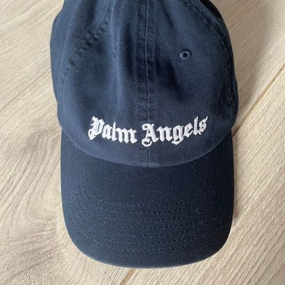 Navy blue cap with 'Palm Angels' logo on a wooden surface
