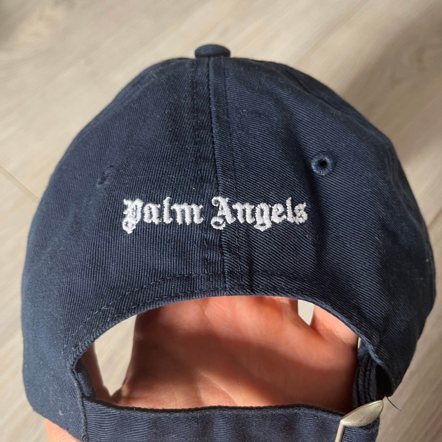 Navy blue cap with 'Palm Angels' logo on a light wooden surface