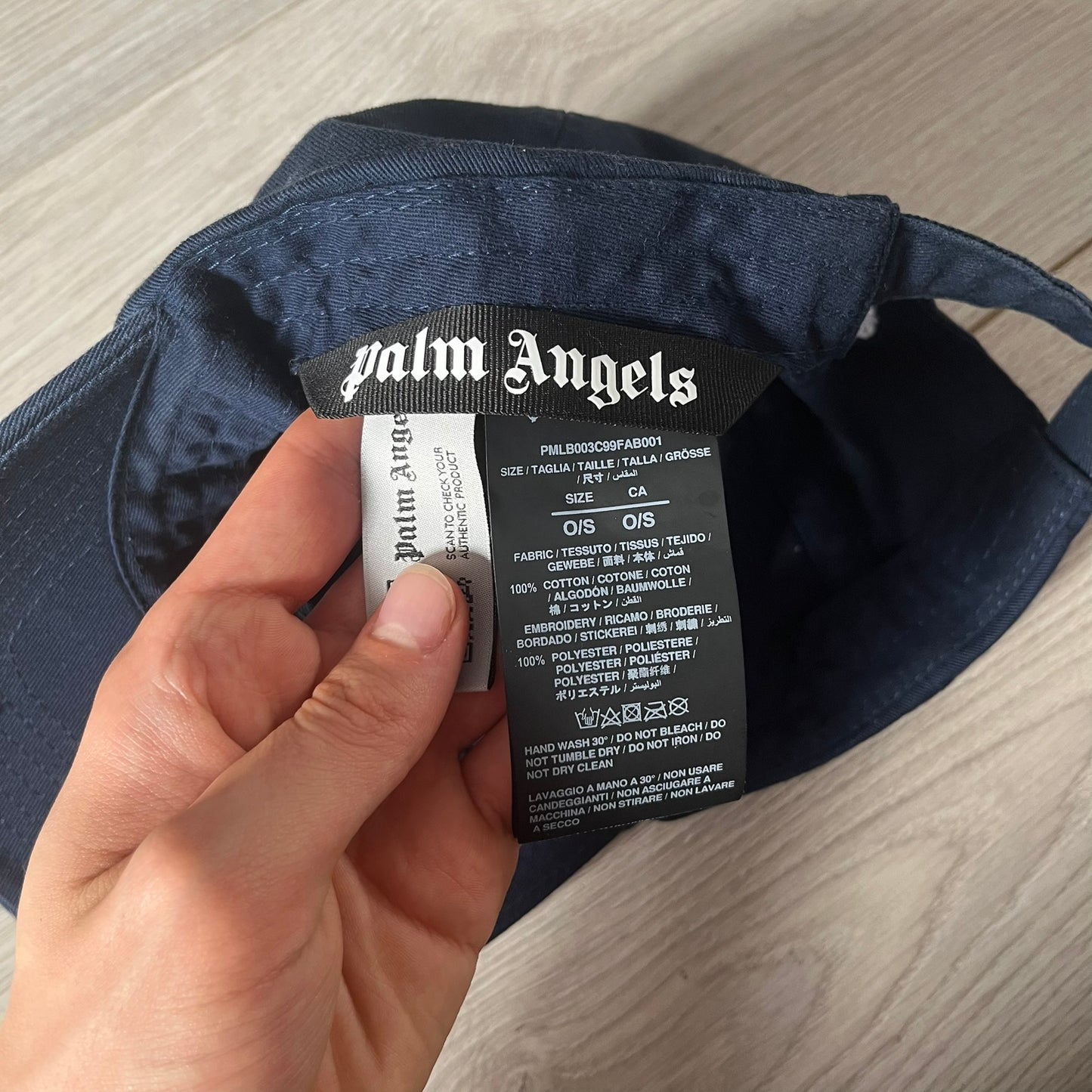 Navy cap with Palm Angels label held by a hand on a wooden surface