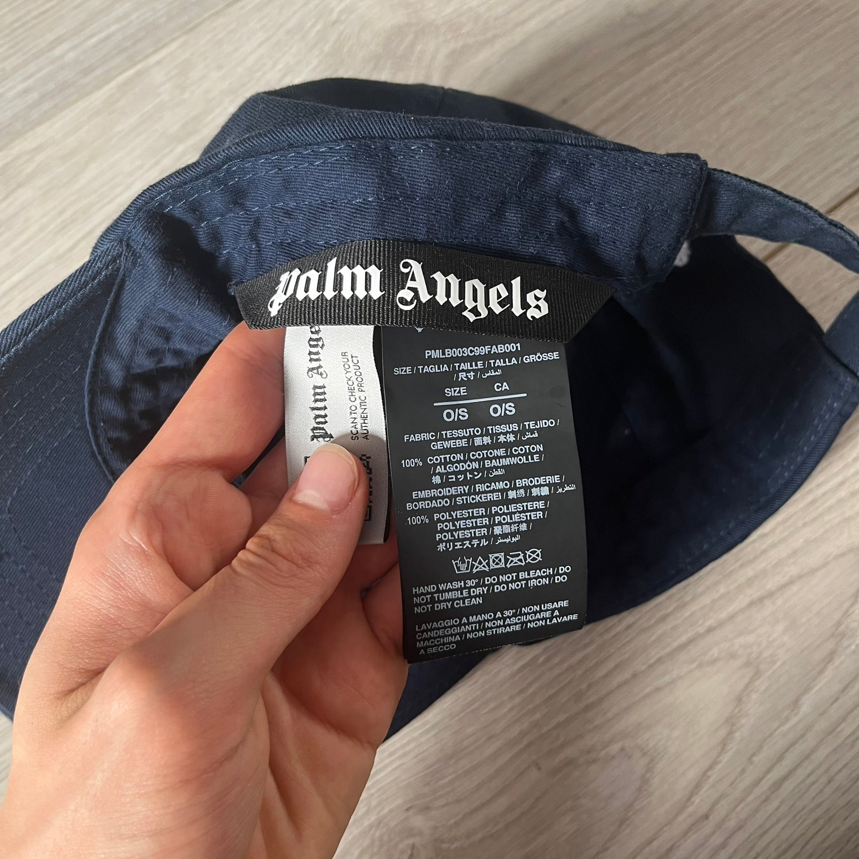 Navy cap with Palm Angels label held by a hand on a wooden surface
