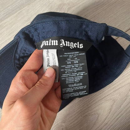 Navy cap with Palm Angels label held by a hand on a wooden surface
