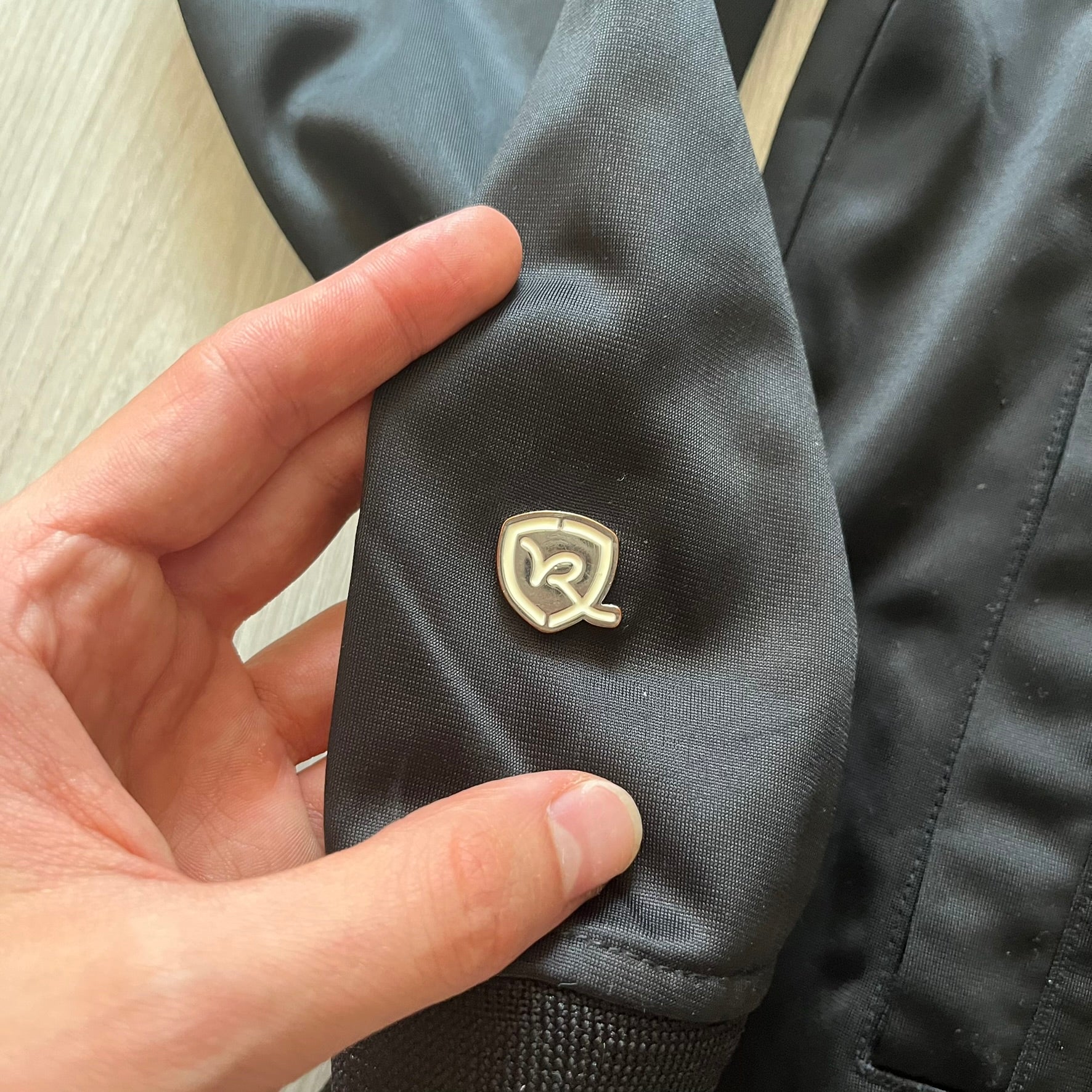 Hand holding a dark jacket with a logo on a light background