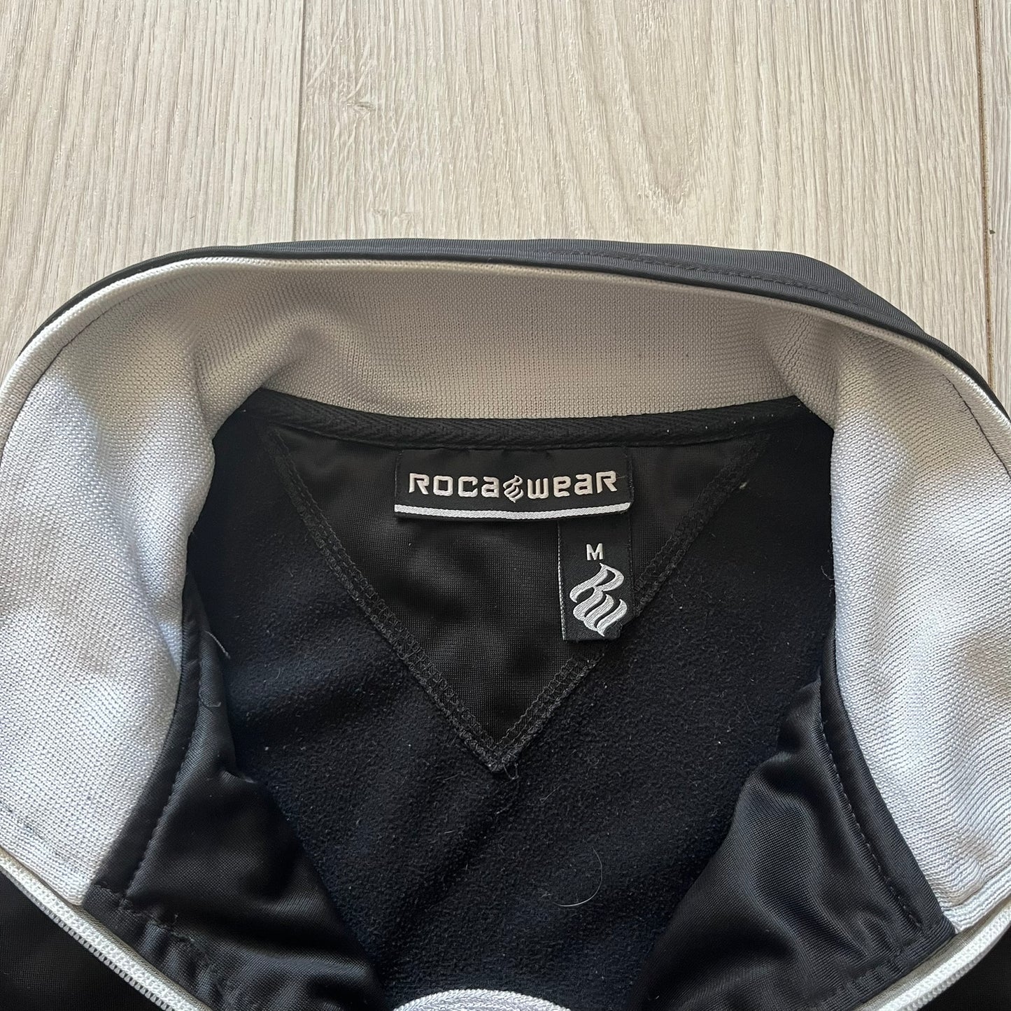 Black garment with Roca Wear label inside a bag on a wooden surface