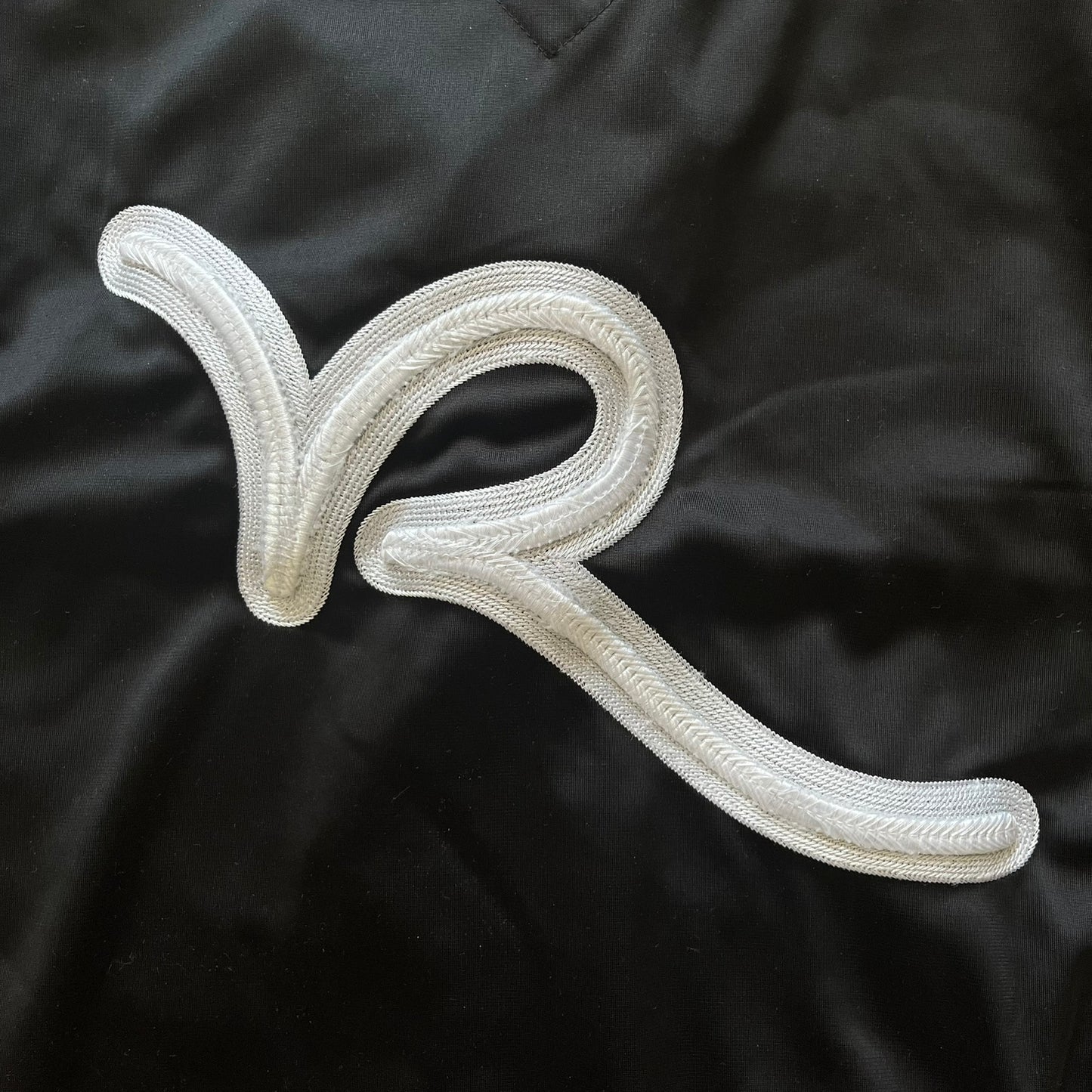 White embroidered letter 'R' patch on a black fabric background