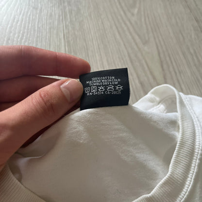 Hand holding a clothing label on a white garment with a light wooden surface in the background