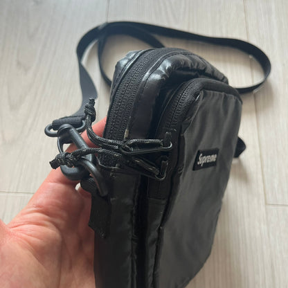 Black Supreme bag held by a hand on a light wooden floor.