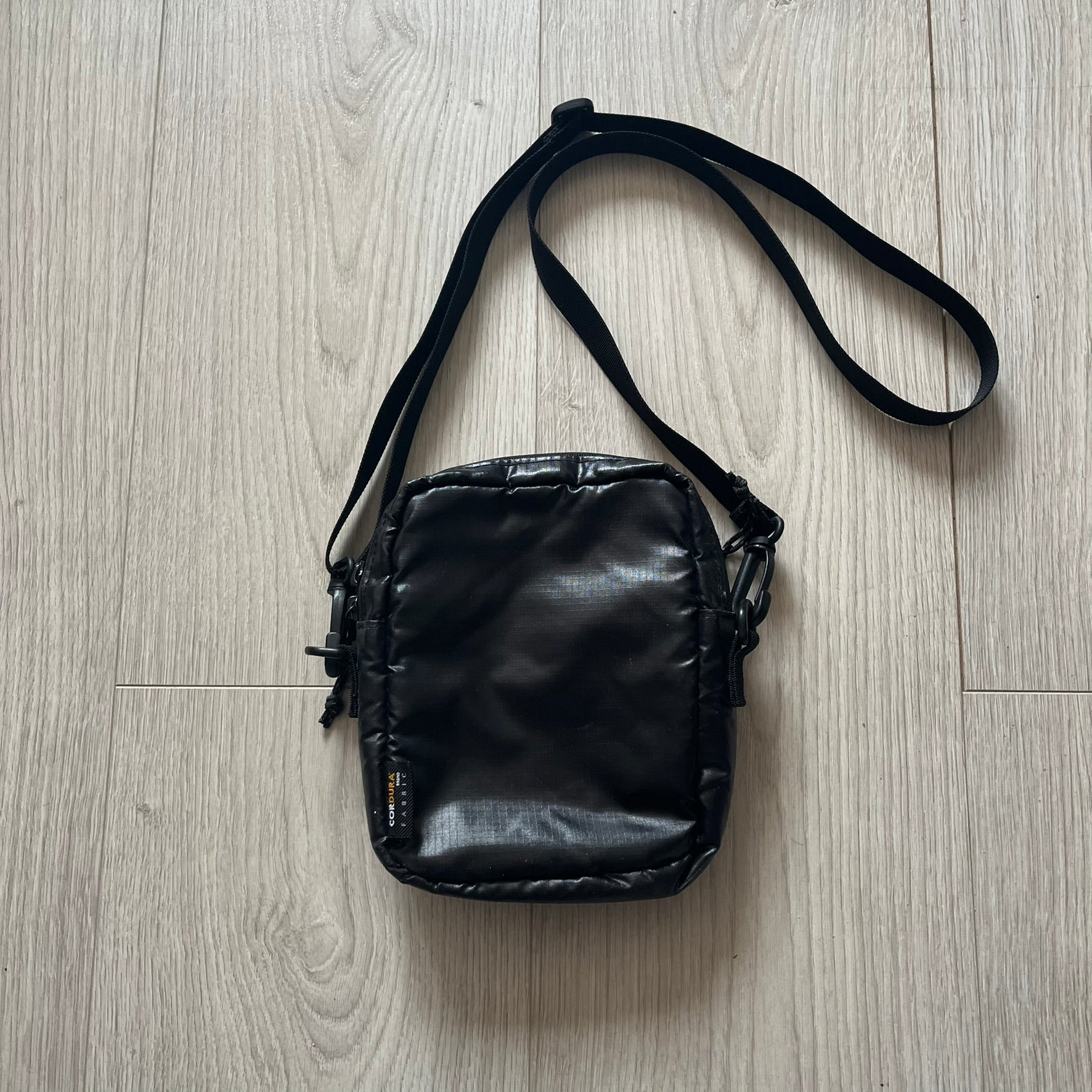Black leather crossbody bag on a light wood floor