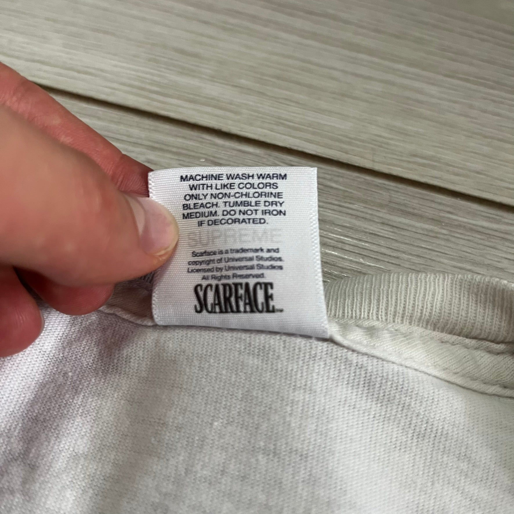 Close-up of a 'Scarface' label on a garment with a hand holding it.