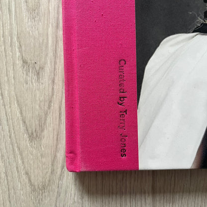 Pink book with 'Curated by Terry Jones' text on a wooden surface