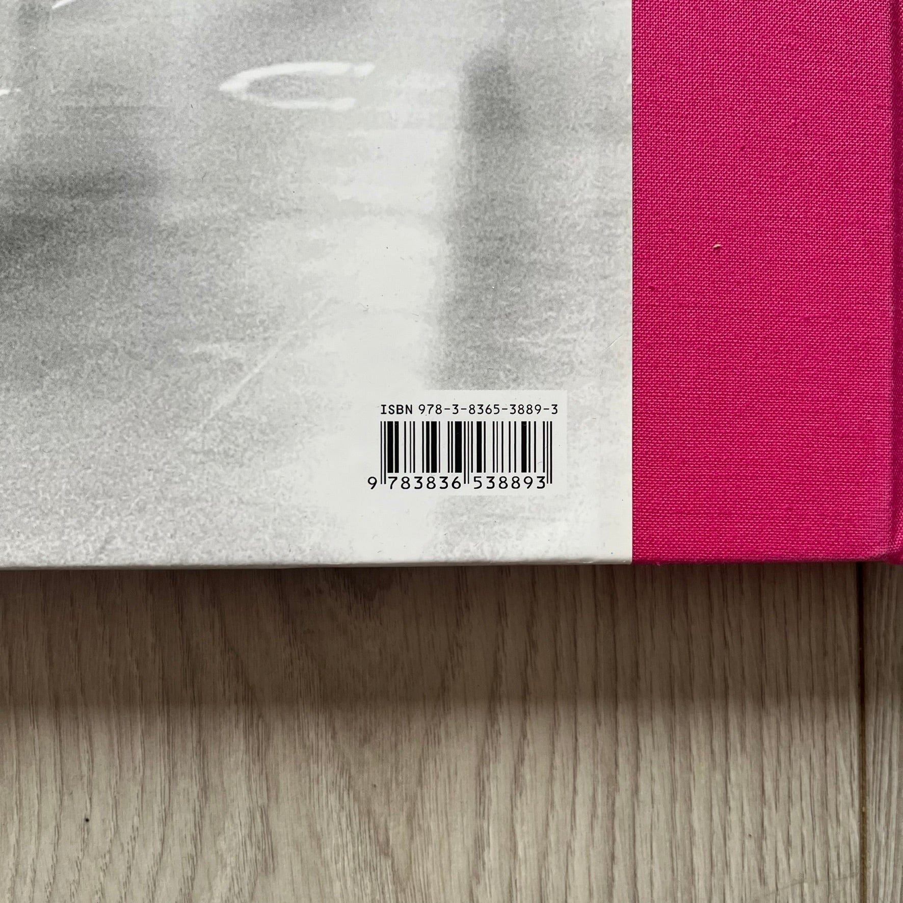 Close-up of a book with a pink cover and a visible ISBN label on a wooden surface.