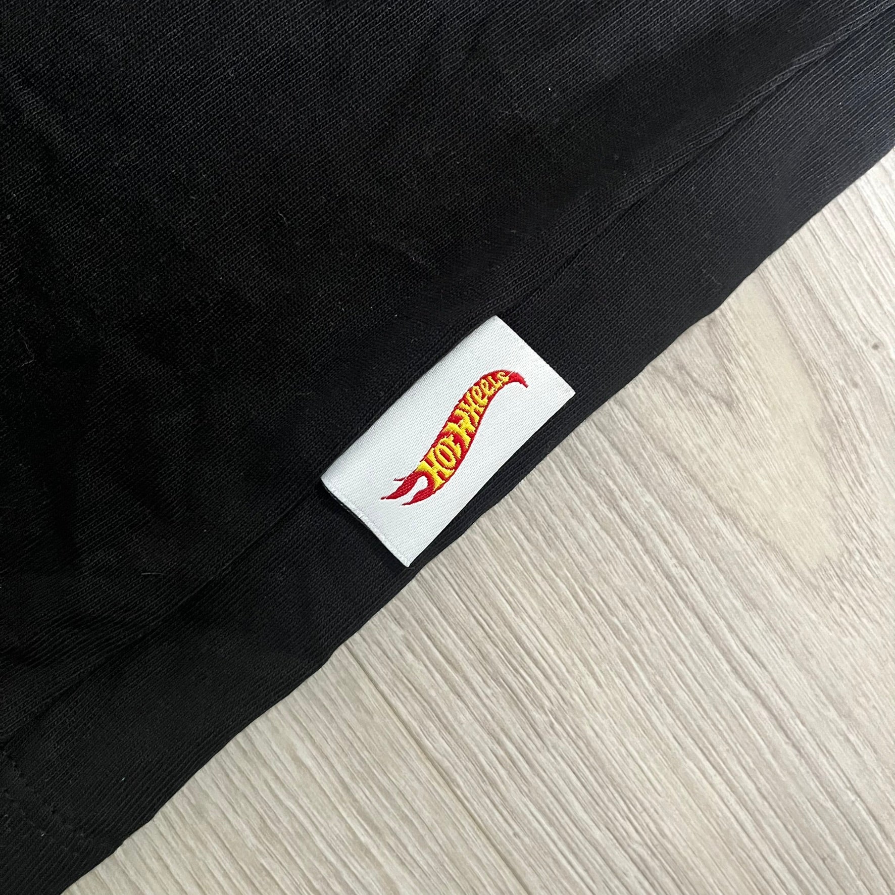 Black fabric with a Hot Wheels logo tag on a light wood floor.