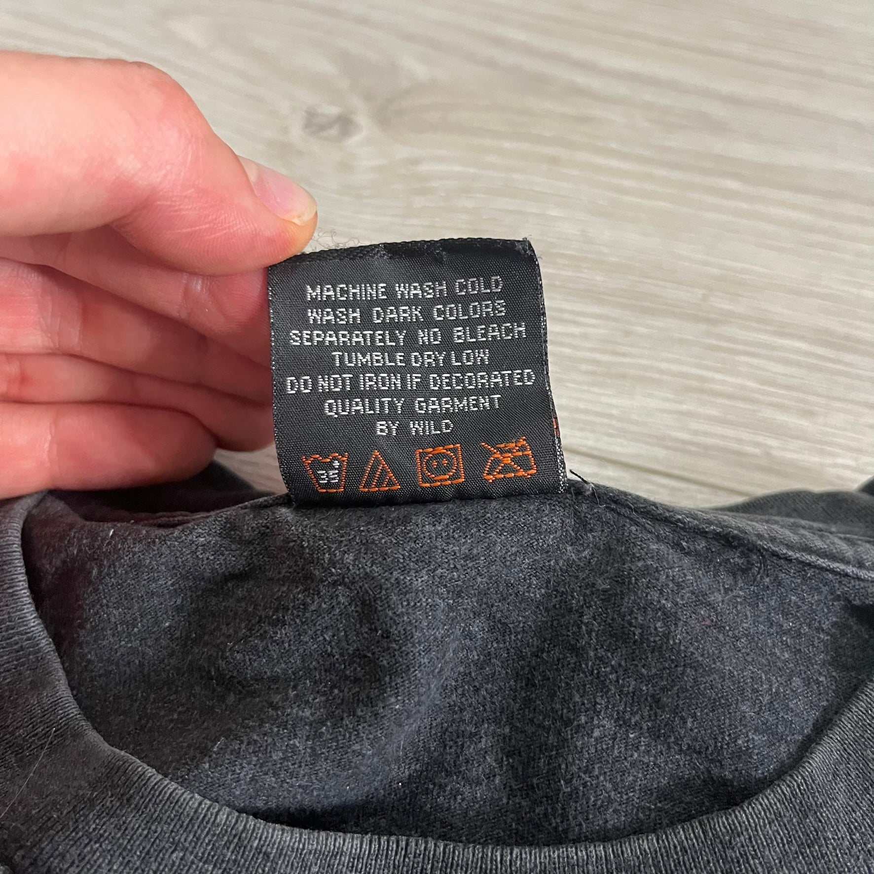 Clothing label with care instructions held by a hand against a neutral background