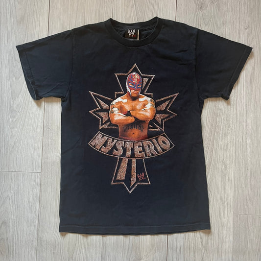 Black t-shirt with a graphic of a wrestler and 'Mysterio' text on a wooden floor.